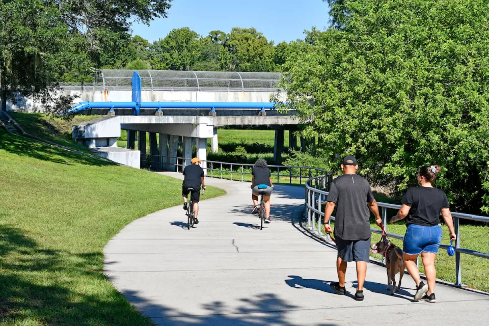 Concrete bike and pedestrian trail with people walking and biking under pedestrian bridge in Orlando, Florida.