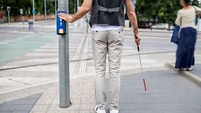 Pedestrian holding visual impairment cane pressing crosswalk button.