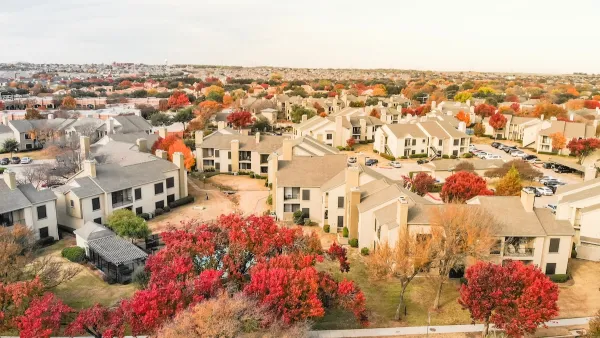 Aerial view of large complex of apartment buildings surrounded by fall foliage trees in suburban Dallas, Texas.