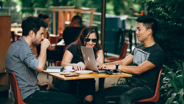 Three young people sitting at a table at outdoor restaurant, one has Apple laptop open.