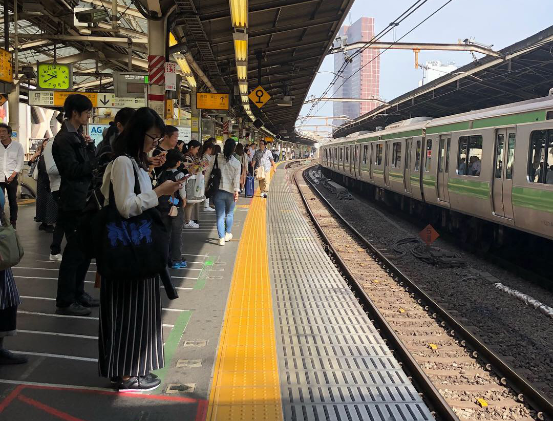 Numerous people line up to use transit at a station in Tokyo.