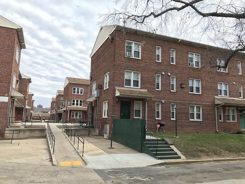 Three-story red brick apartment building with wheelchair ramp leading to side of building in Baltimore, Maryland. Part of Poe Homes public housing development.