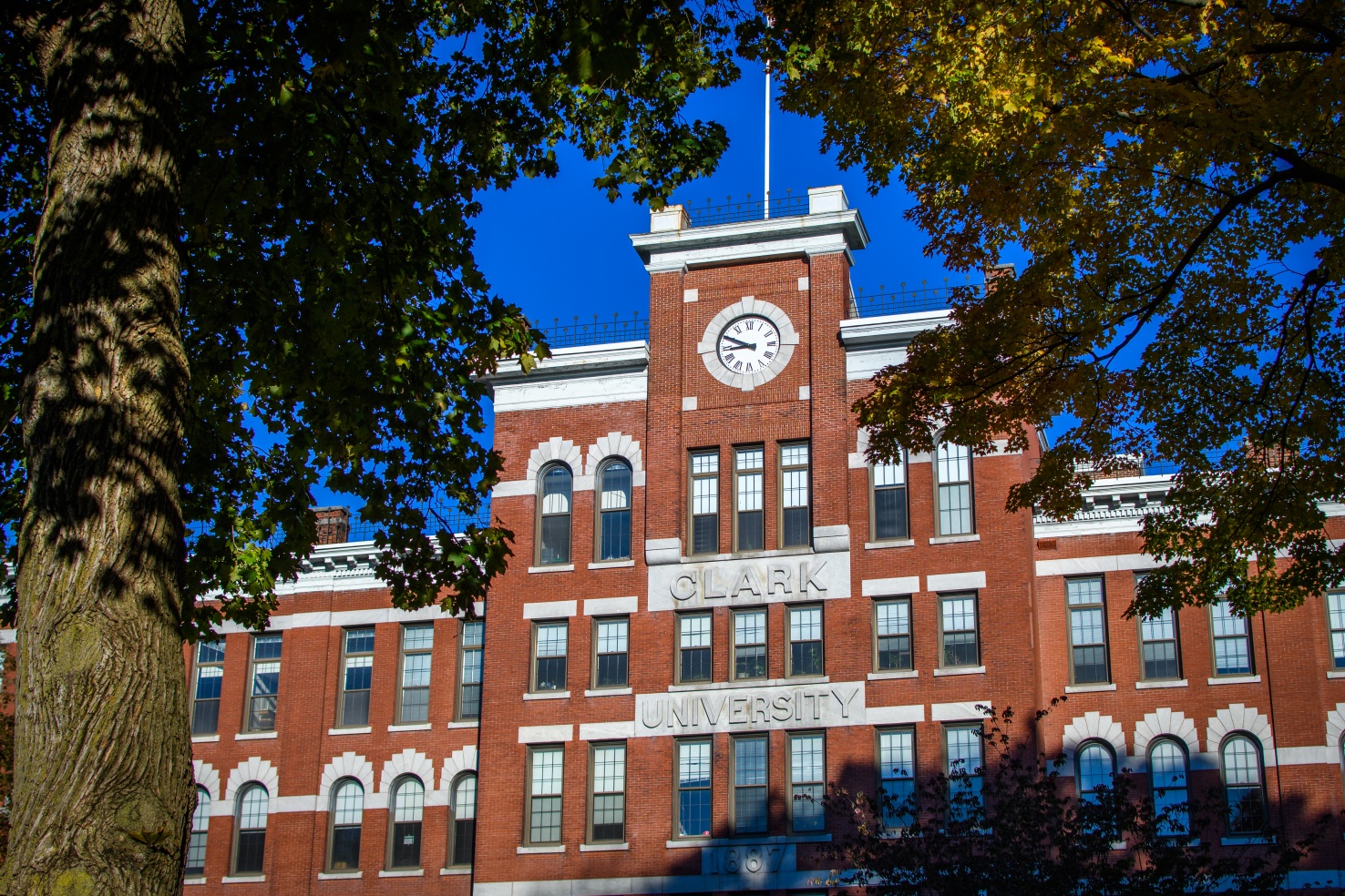Image of a brick building with a clock face on it with cement sign saying Clark University on it