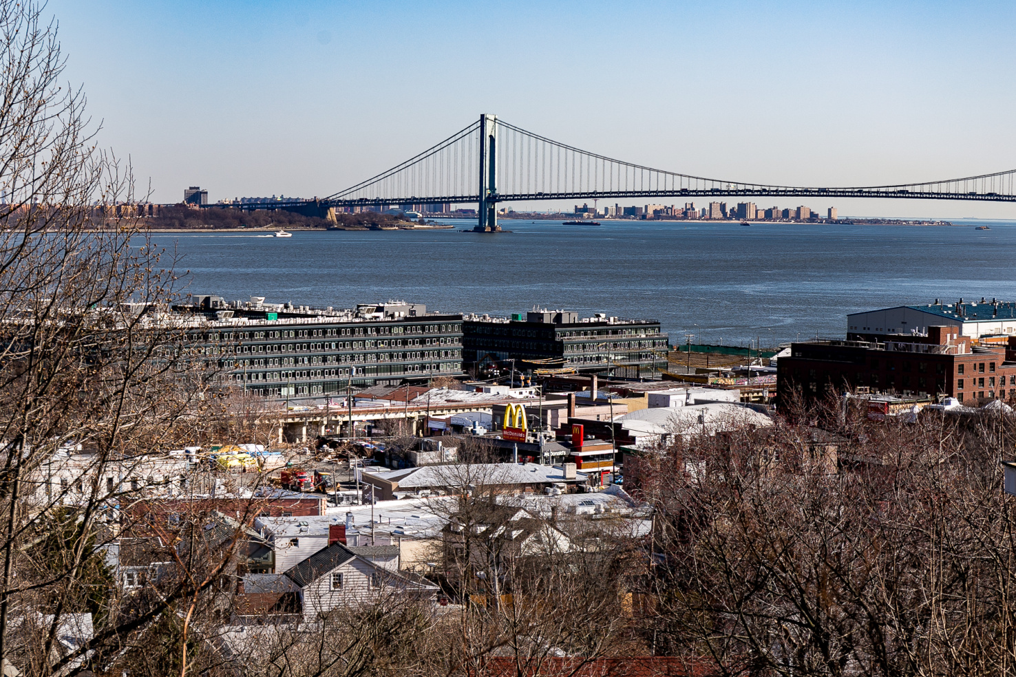 A green bridge is in the distance, bare trees are in the foreground. An apartment complex is visible between them.