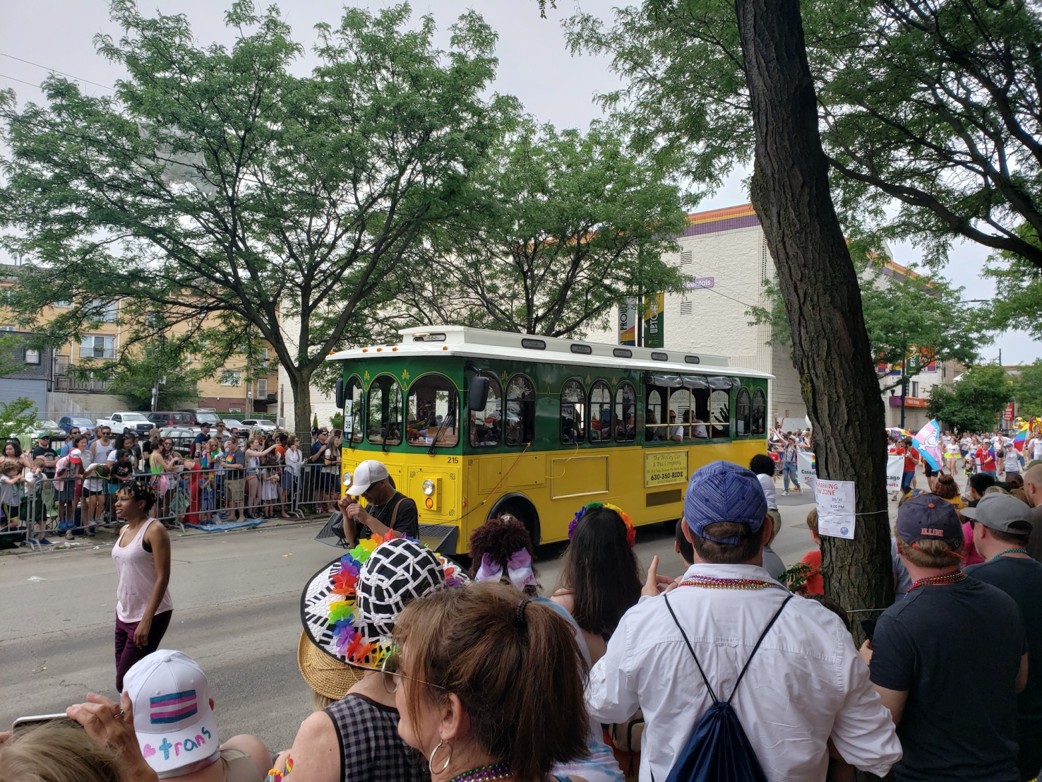 Green and yellow trolley moving down street as seen from a crowd on the sidewalk.