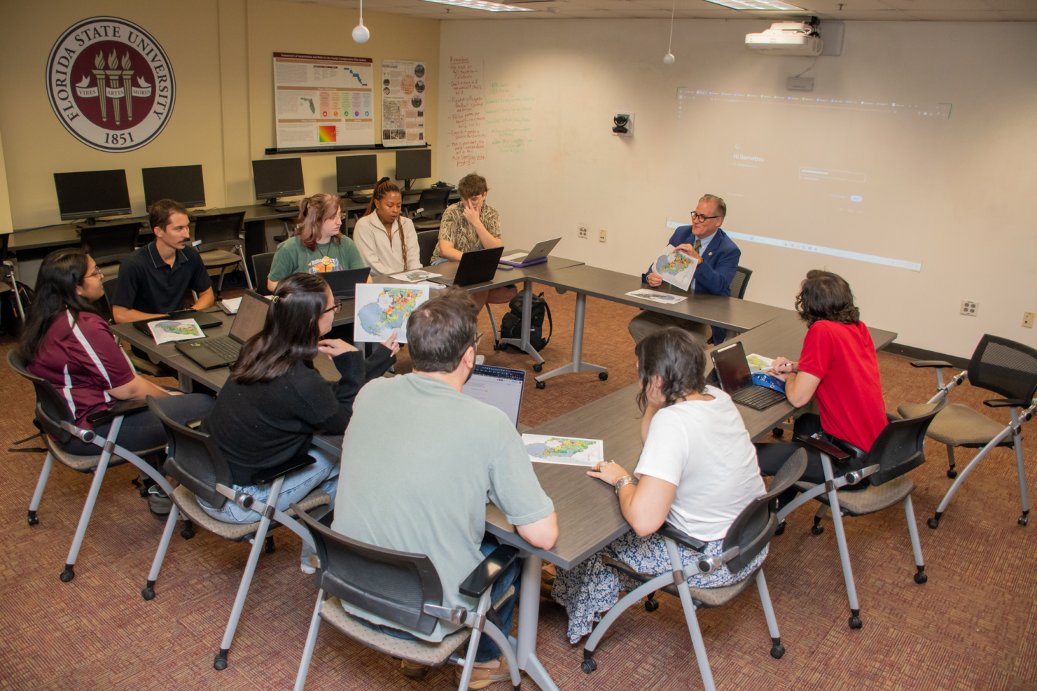 Group studio class image of students and professor sitting in a square table formation