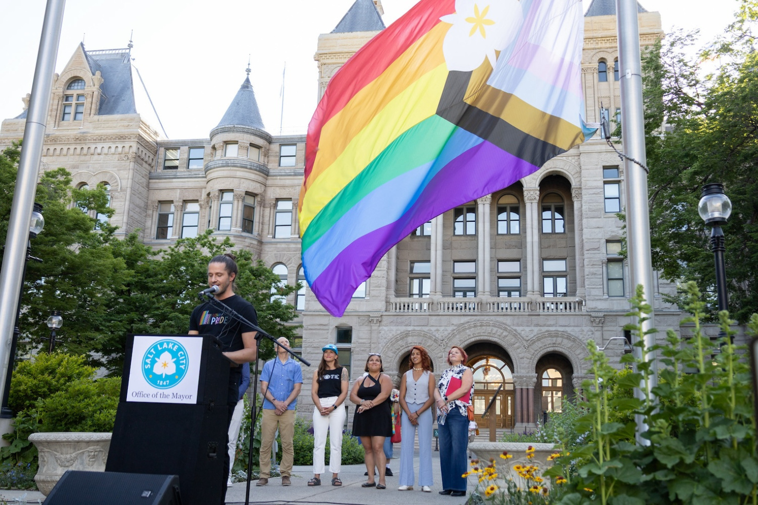 People stand in front of Salt Lake City Hall presenting new LGBTQ-supportive city flag.