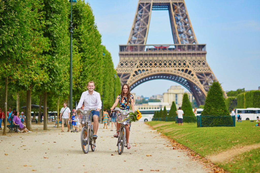 Cheerful man and woman riding bikes in Paris, France with Eiffel Tower in background.