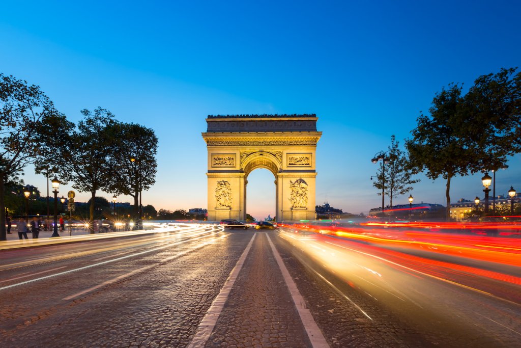 Arc de Triomphe in Paris, France at night with blurred car lights speeding past.
