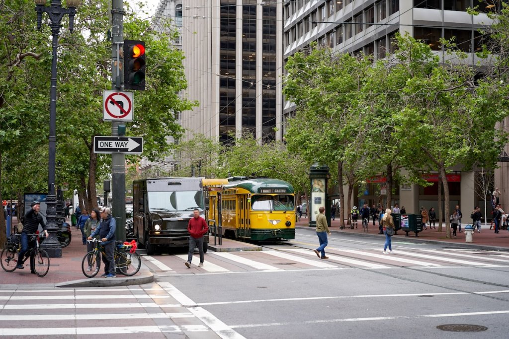 Vintage yellow streetcar and people walking at intersection in San Francisco, CA.