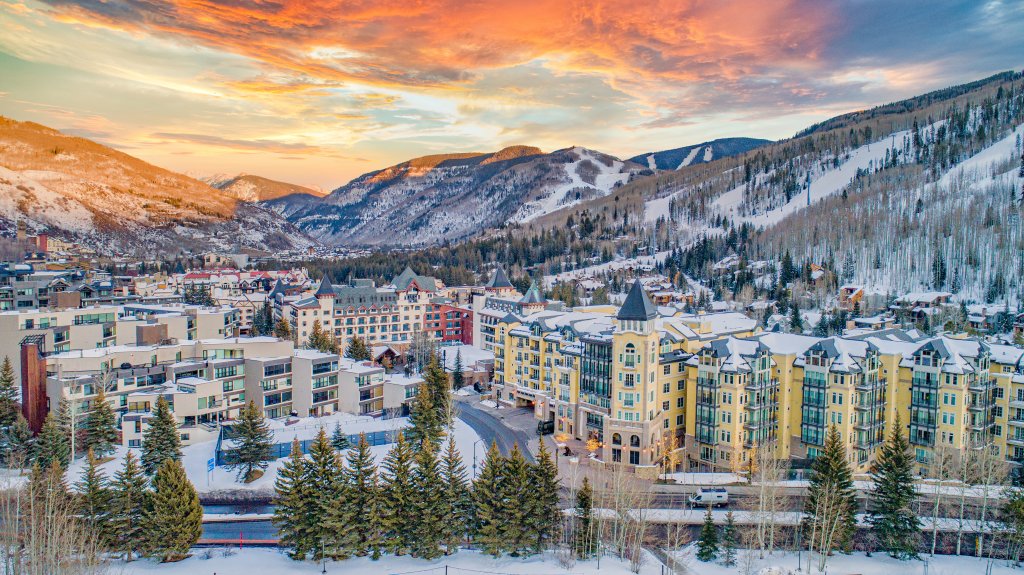 Large multifamily residence and hotel buildings in snowy valley, surrounded by mountains.