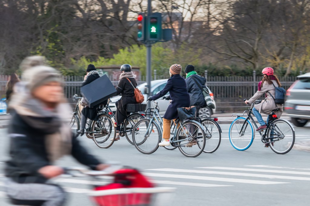 A half-dozen cyclists pedal through an intersection, which has a traffic light with a figure of a bike lit up in green.
