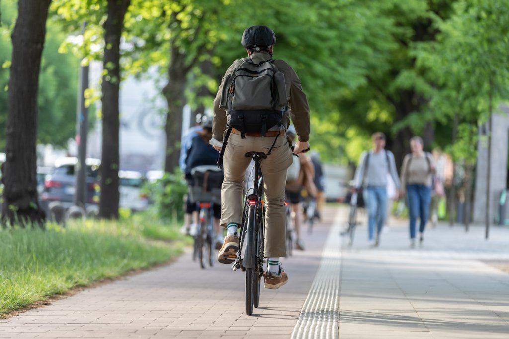 View from behind of man biking on separated bike route and people walking in background.