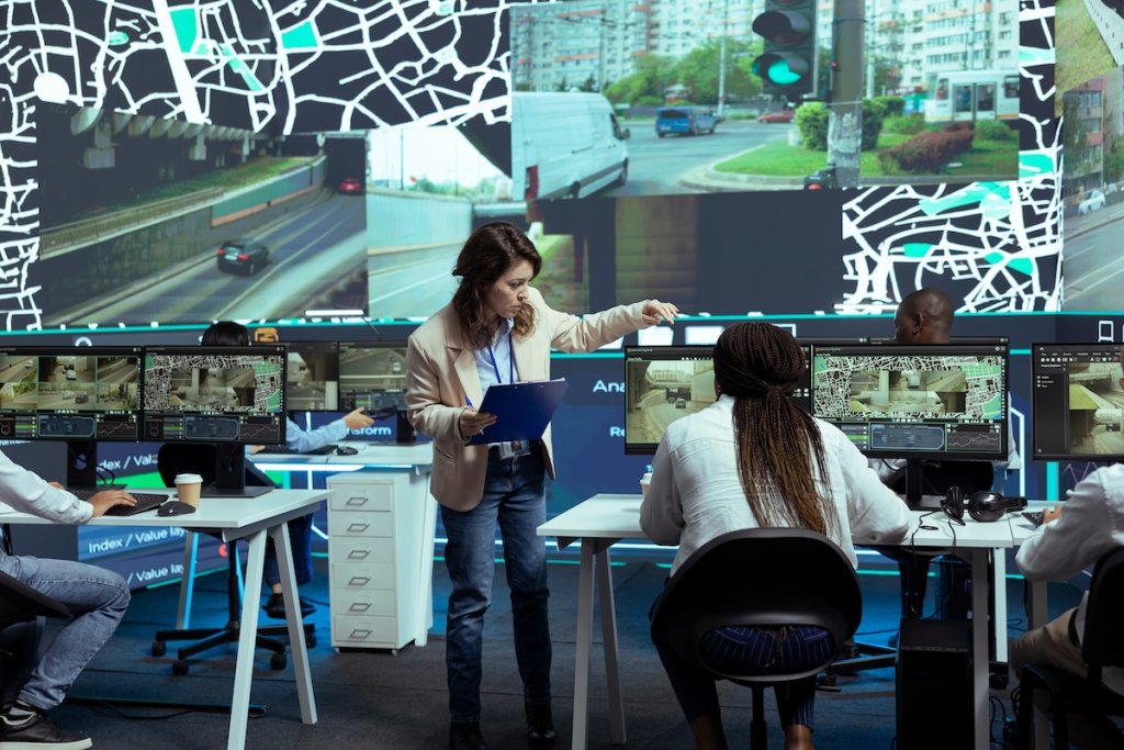 Two women working at computers in room with many monitors on desks and on wall showing maps.