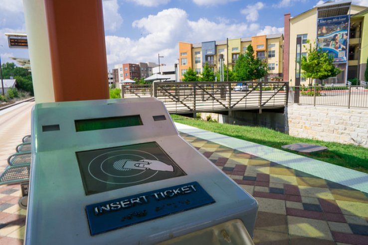 A fare-card reader is shown at an Auston rail station, with brightly colored apartment buildings in the background.