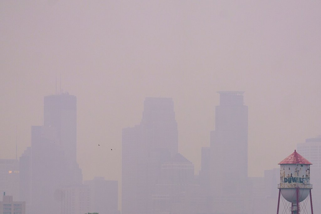 The Minneapolis downtown building is barely visible through wildfire smoke with a water tower in the foreground on the bottom right.