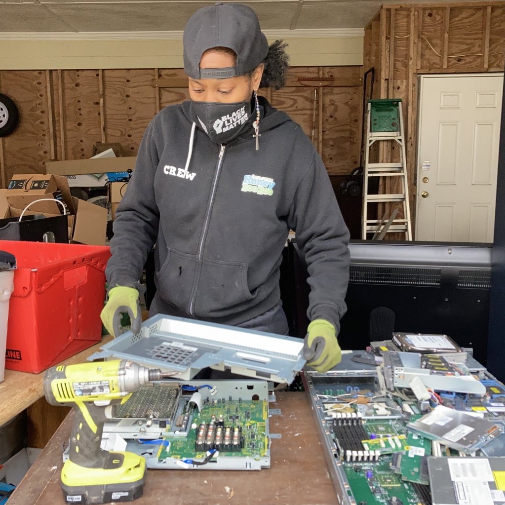 An image of a Black women working to prepare electronic parts for recycling.