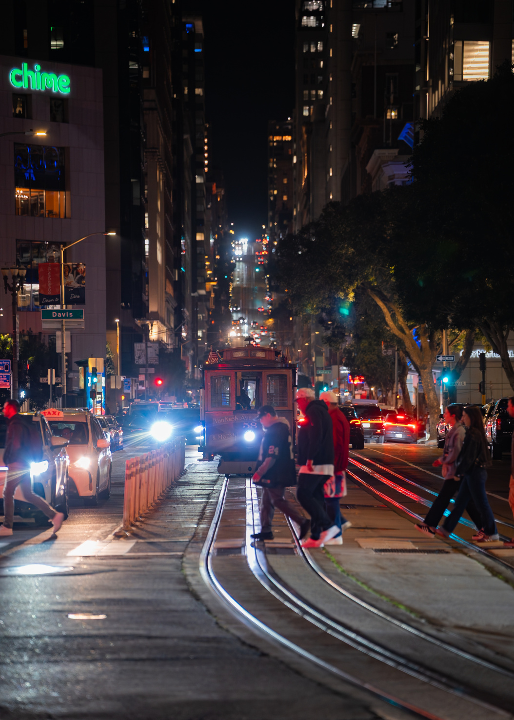 People walking on street behind classic cable car in San Francisco at night.