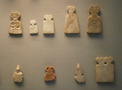 Two rows of tan eye idols. The eye idols have two overside eyes at the top, with a thin neck and broader body.