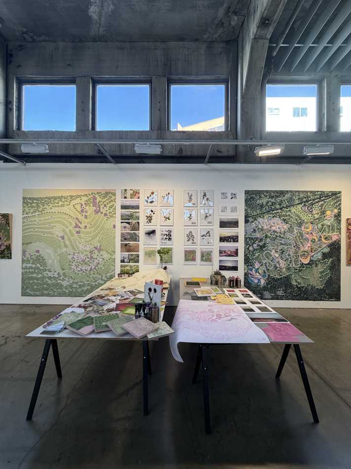 Image of an empty space of a classroom with a table in the middle with several different peices of art, photos, paintings, books etc. Walls in the background have large images of landscape maps