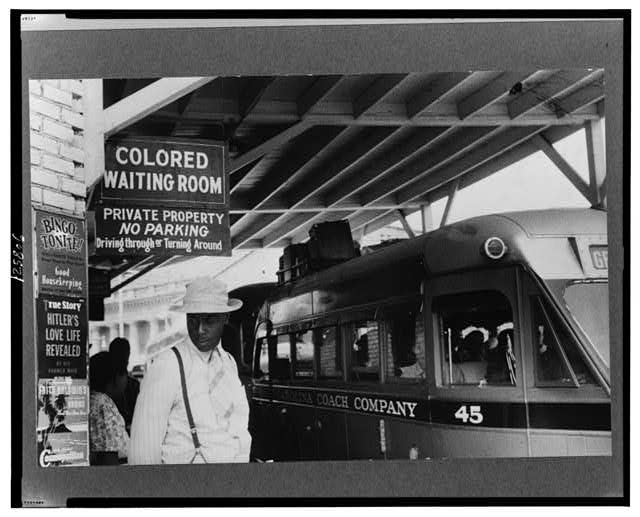 Black man waiting under "Colored Waiting Room" sign at train station in Durham, North Carolina.