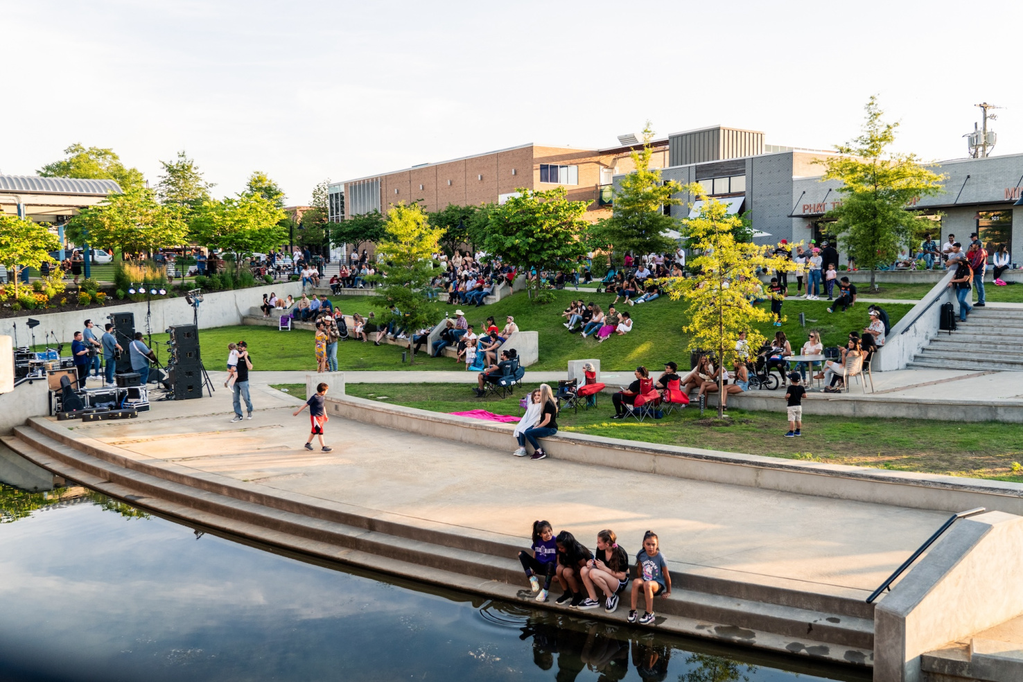 People sitting and walking on a concrete walkway in a public park in Springdale, Arkansas.