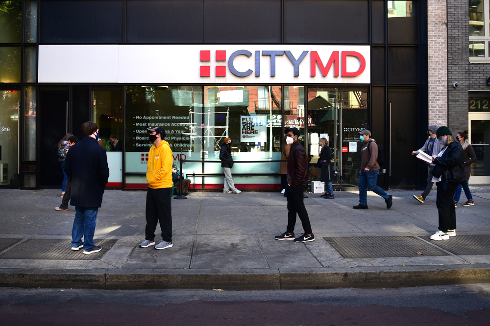 A New York street during the Covid-19 pandemic in front of a “City MD” store. people are wearing masks and waiting in socially distanced lines.