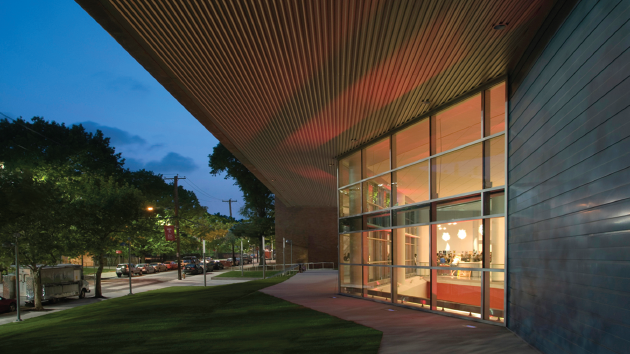 Tyler building during dusk with bright big windows from floor up illuminated with a large overhang roof and lawn