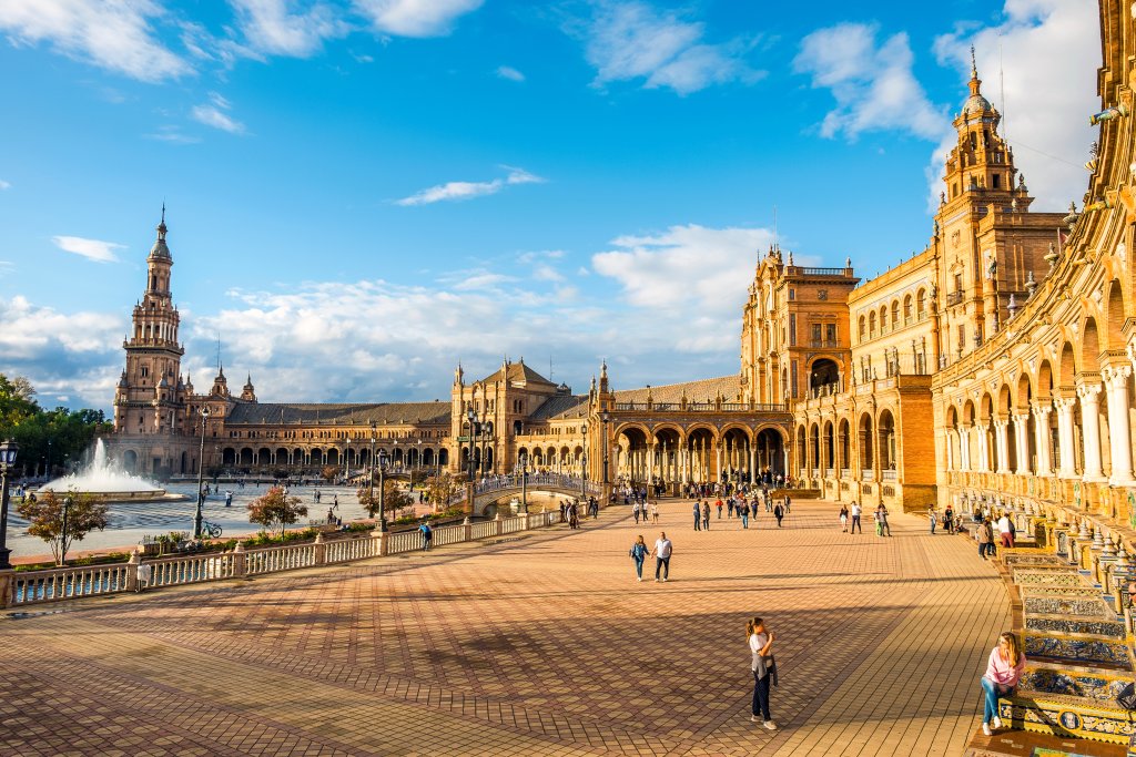 Wide curved stone walkways around massive courtyard on left and stone structures on right with tourists walking around.