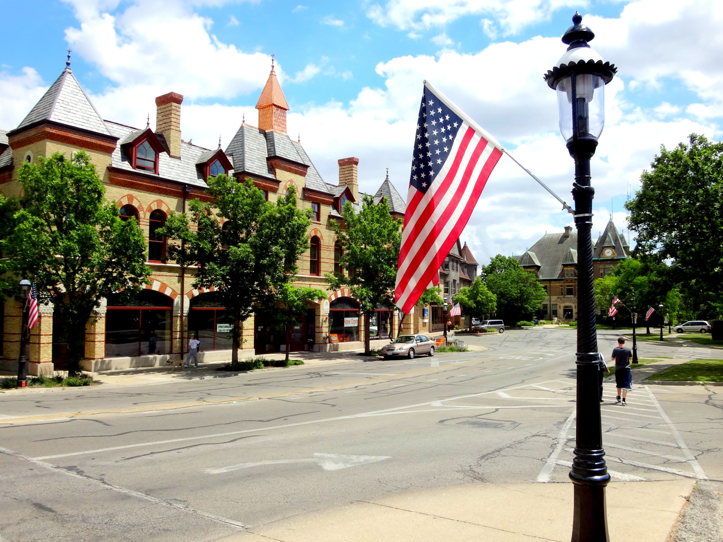 An American flag on a lamppost, in front of a yellow building with several pointed towers.