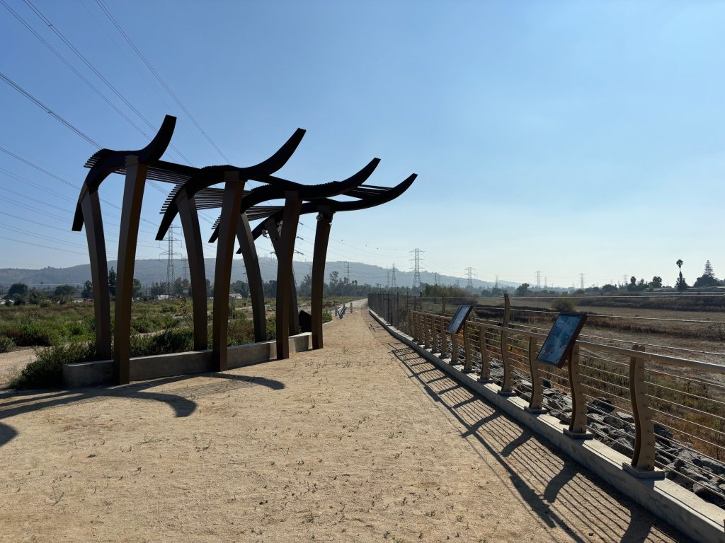 A walking path with a metal sculpture alongside a dry riverbed.
