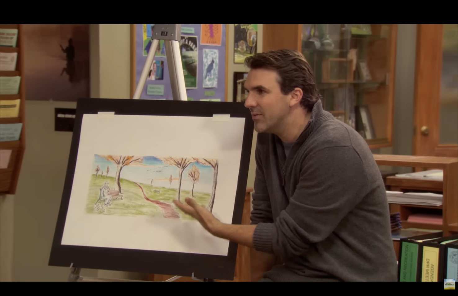 Screen shot of city planner pointing at board with painting of park in Parks & Recreation.