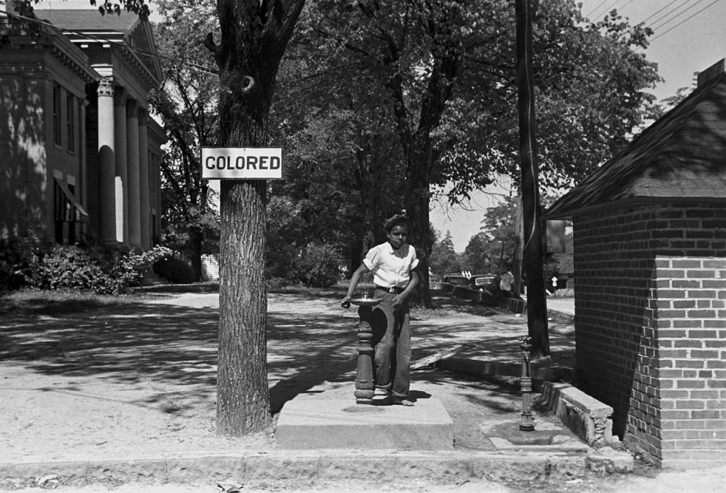 Young Black girl using segregated drinking fountain.