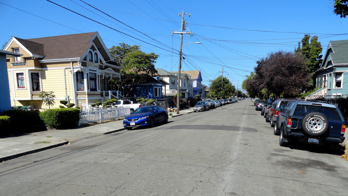 Street with small older wood houses in pastel colors in Oakland, California.