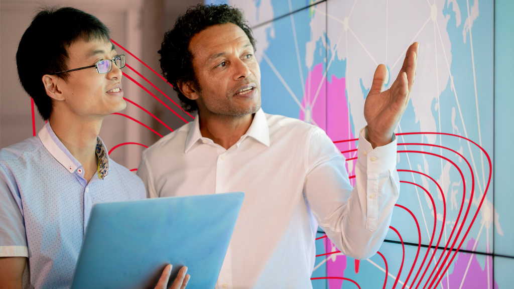 Two men discussing the large map displayed on the screen to their left