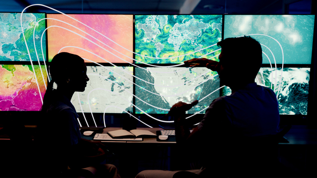 Figures in a dark room in front of rows of screens displaying colorful weather maps of North America and the world
