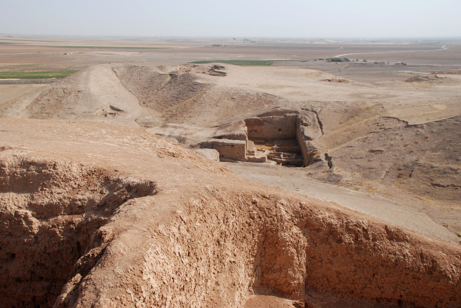 The ruins of Tell Brak. A structure is barely visible amongst tan rock. Two walls and a small window are visible.