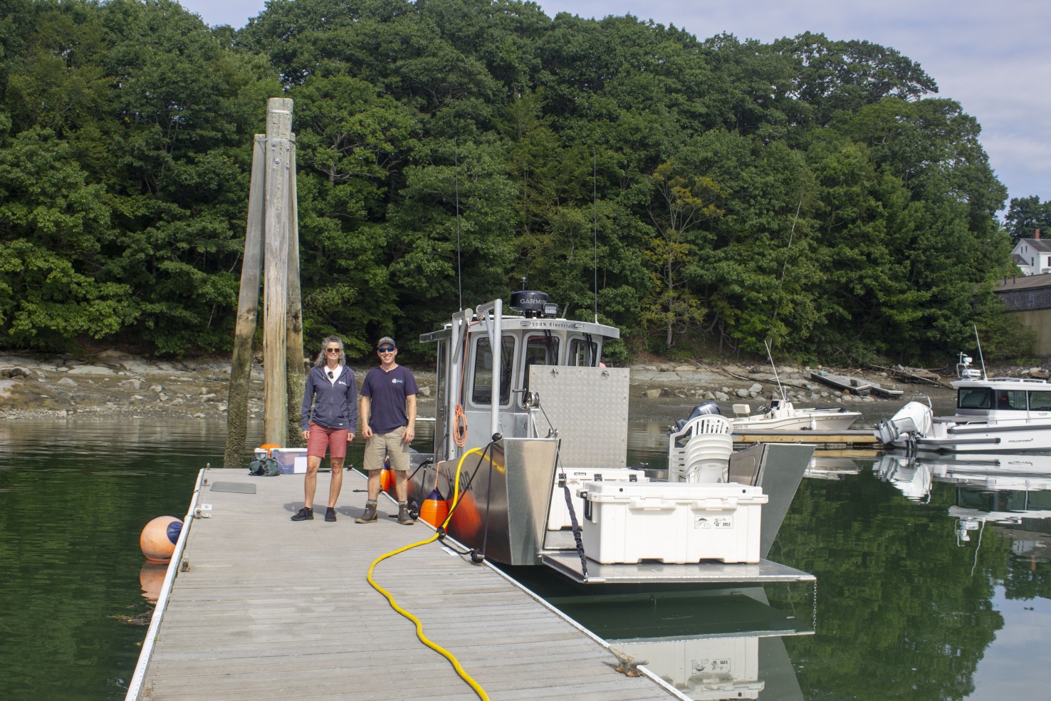 The Island Institute's Lia Morris (left) is working with Willy Leathers (right) and his crew at Maine Ocean Farms to collect performance data on the electric boat Heron, pictured here charging from a low-capacity shoreside power supply at a slip in South Freeport, Maine.