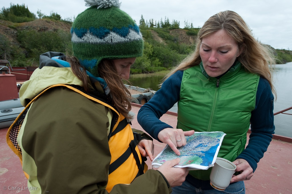 Two women outdoors pointing at a place on a paper printed out map with her pinky finger out on a dock