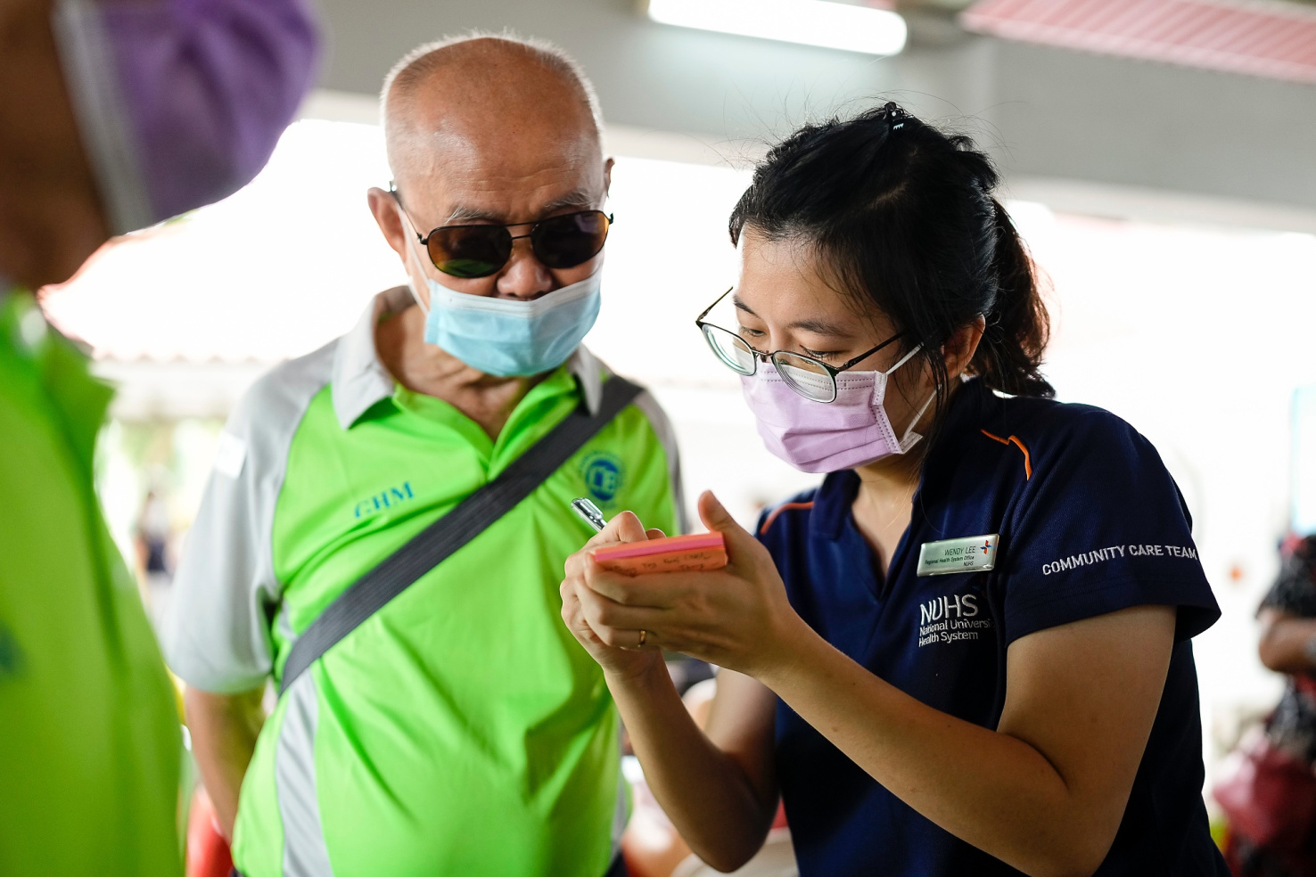 A woman writes something on a post-it note for an older man.