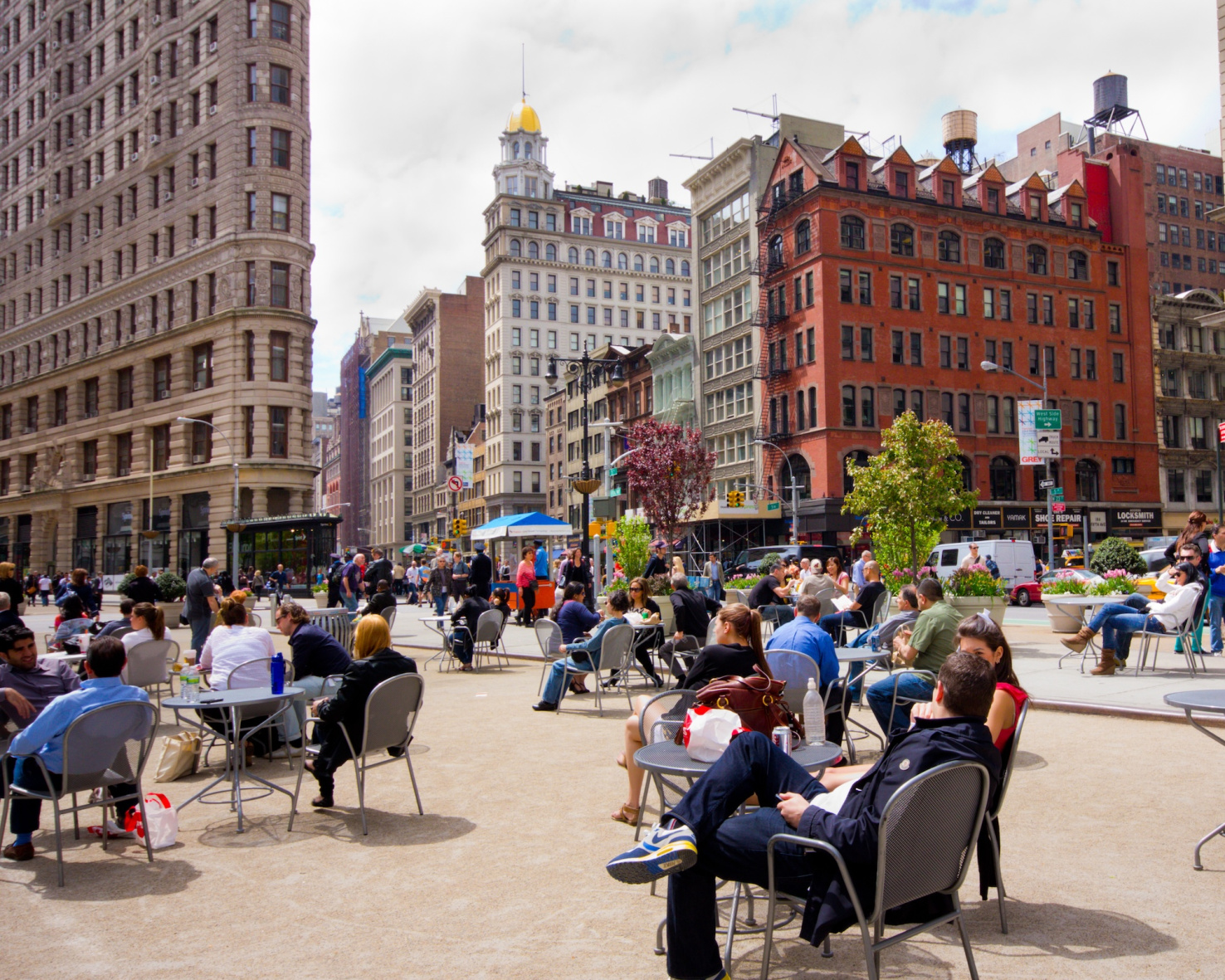 People at tables set up in a public plaza next to the Flatiron Building in NYC.