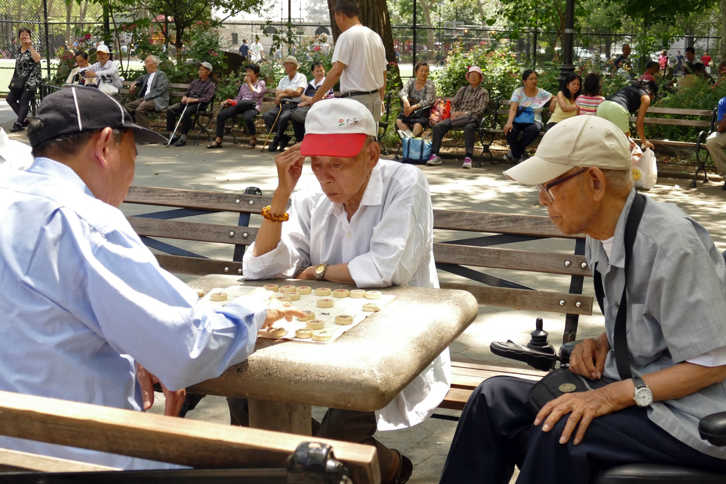 Older Chinese men playing a tile game on a table in a park in New York City.