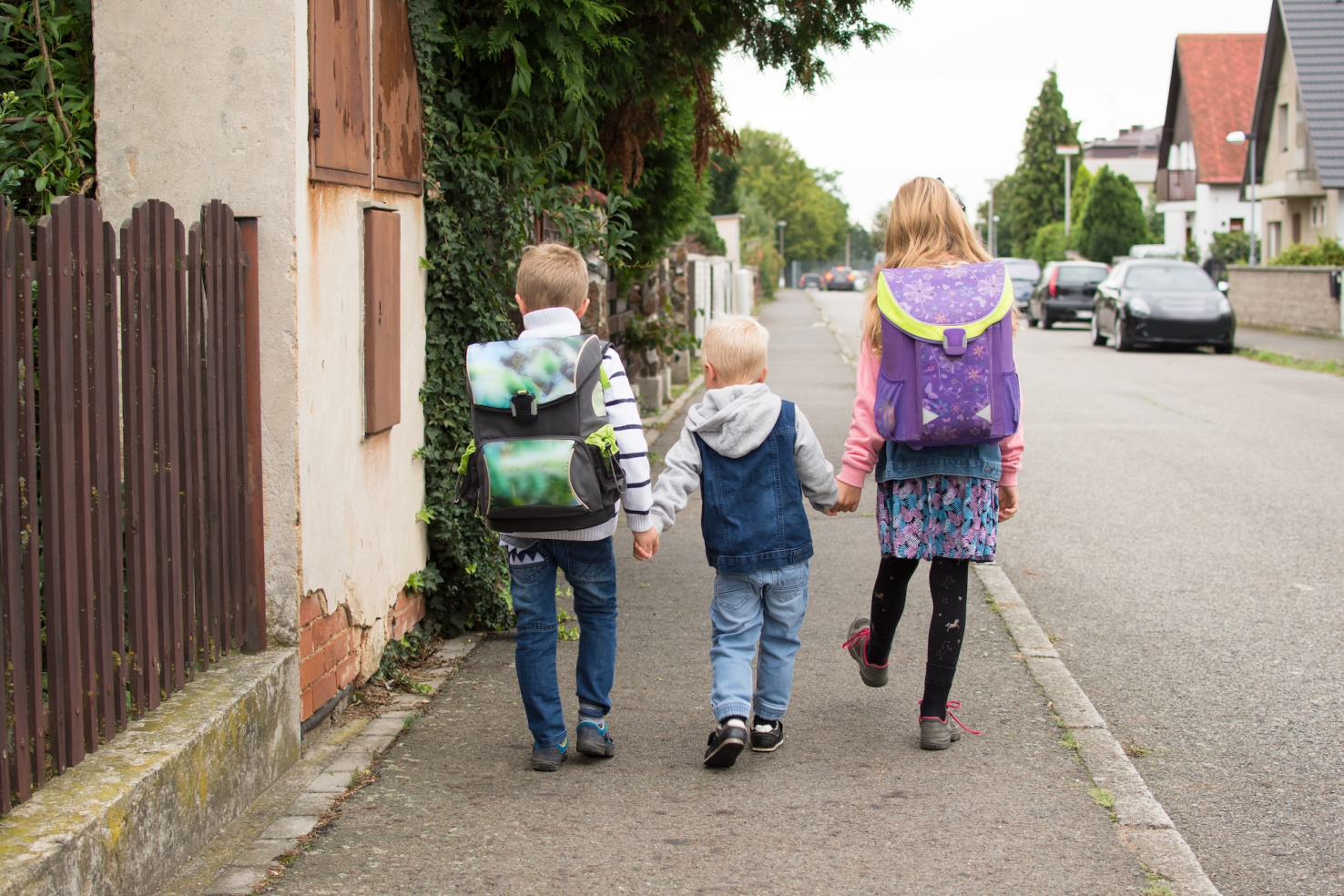 Three young children walking holding hands on small residential street.