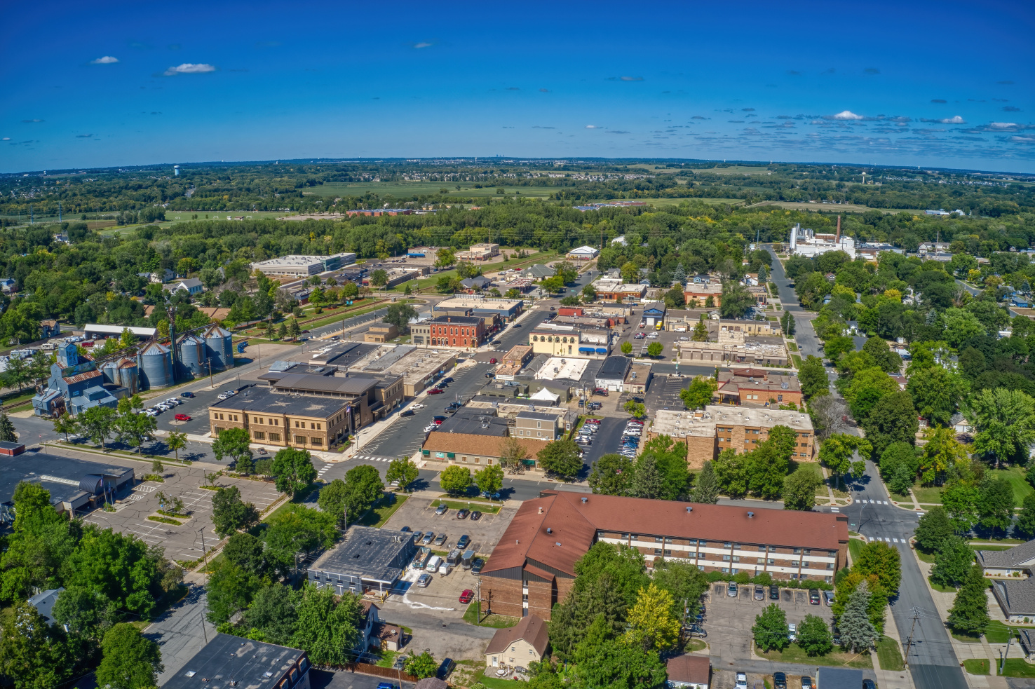 A small town surrounded by trees. There is ample space dedicated to parking lots, and a large, L-shaped, copper-colored building in the bottom right.