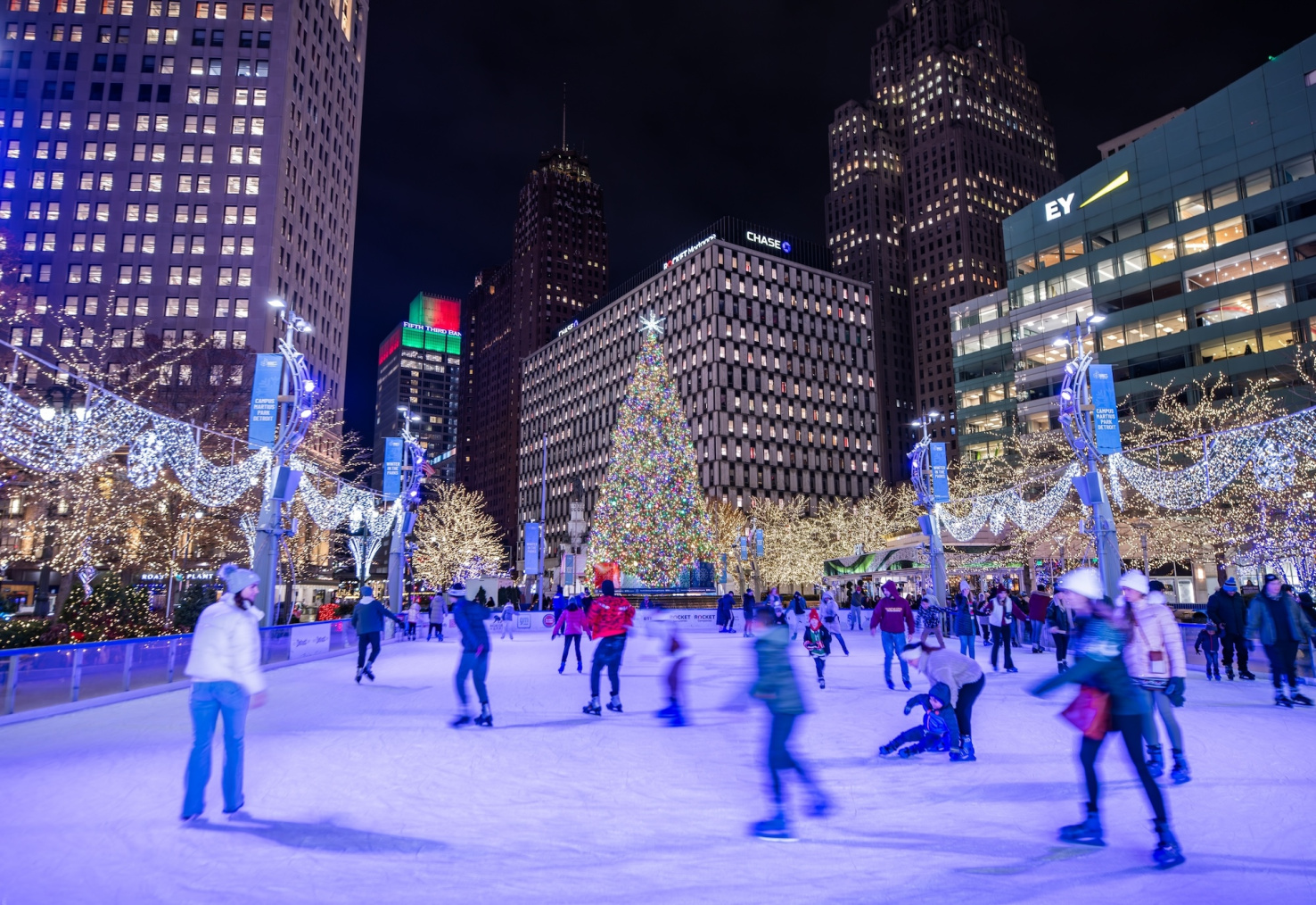 Ice rink with Ice skaters with Christmas tree at Campus Martius Park at night in downtown Detroit, Michigan decorated with holiday Christmas lights
