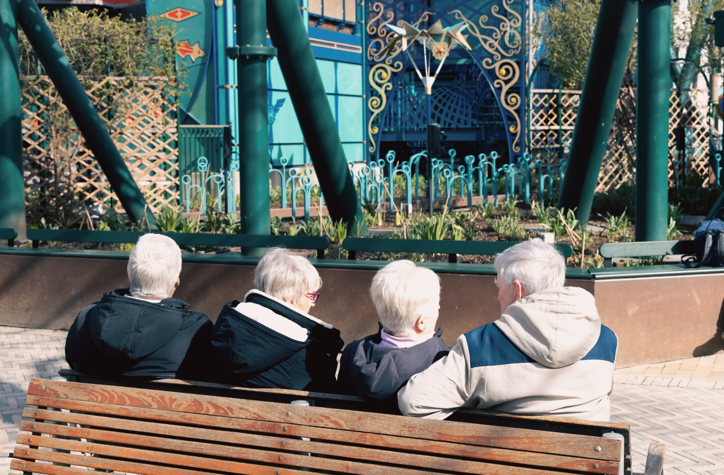 Four elderly people with gray hair are sitting and relaxing on a bench in the park. Retirement lifestyle. Copenhagen, Denmark.