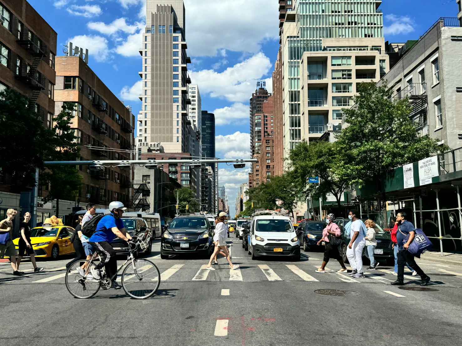 NYC residents cross the street with an automatic congestion pricing toll machine in the background. 