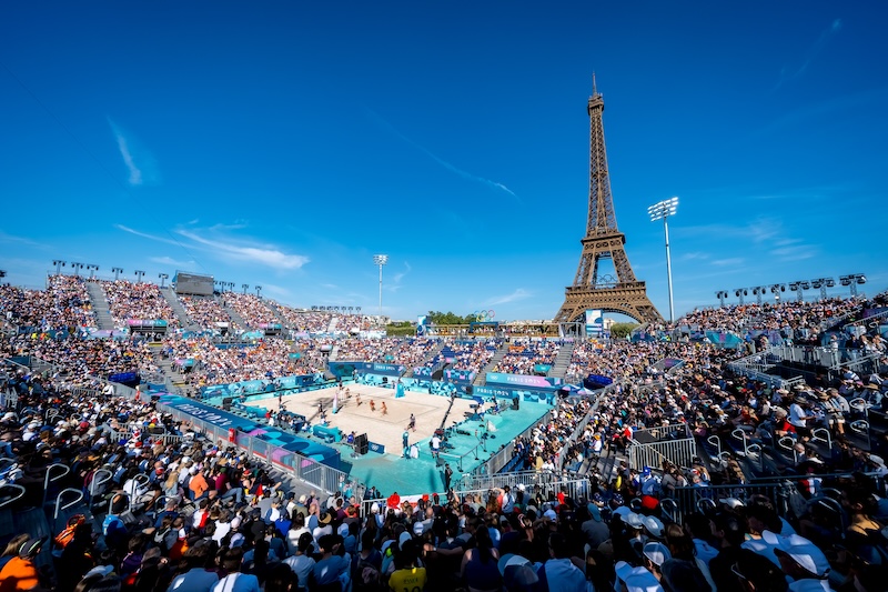 Beach volleyball stadium filled with crowd and Eiffel Tower visible in background in Paris, France.