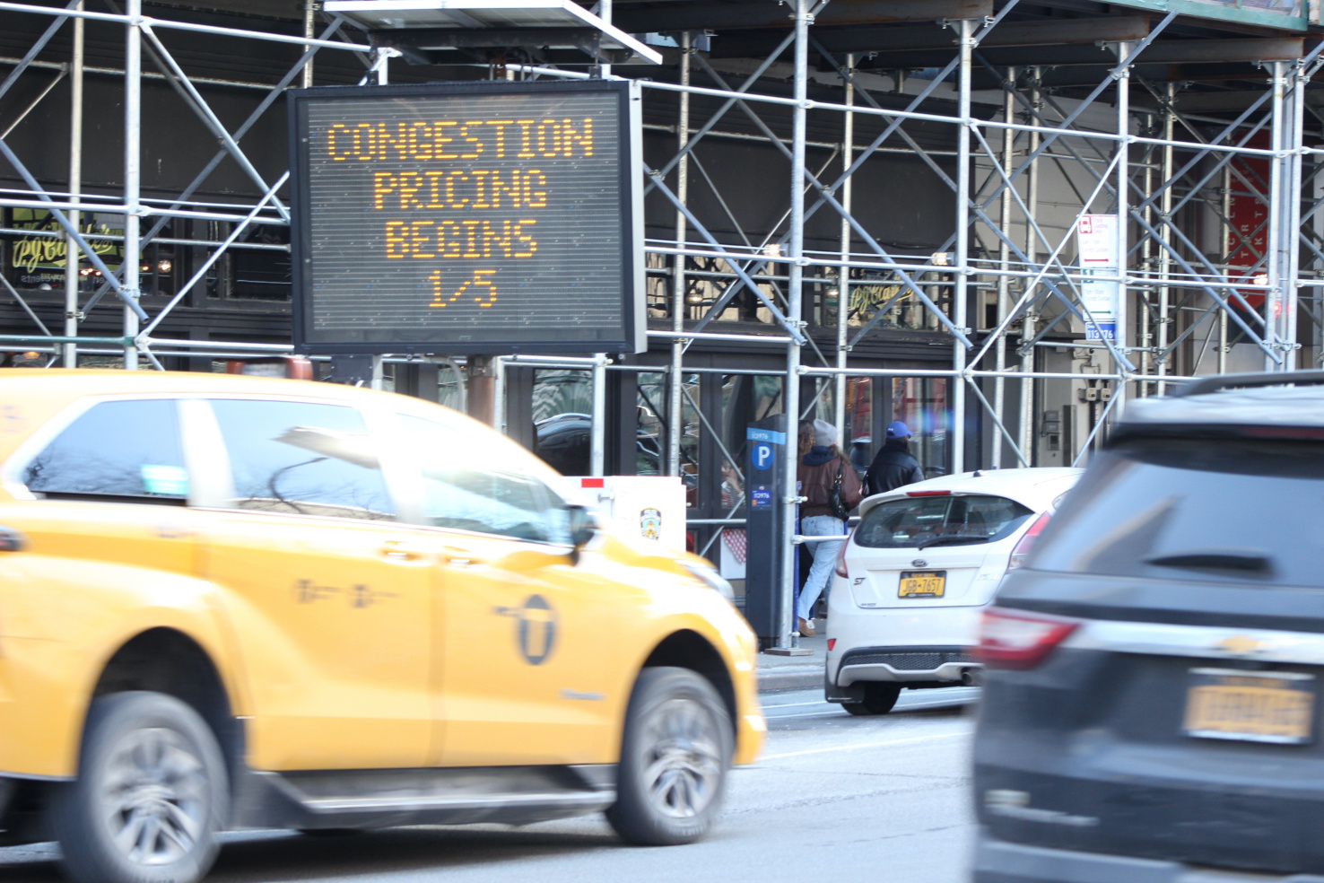 A sign announces the start of congestion pricing on 1/5. Cars drive past.