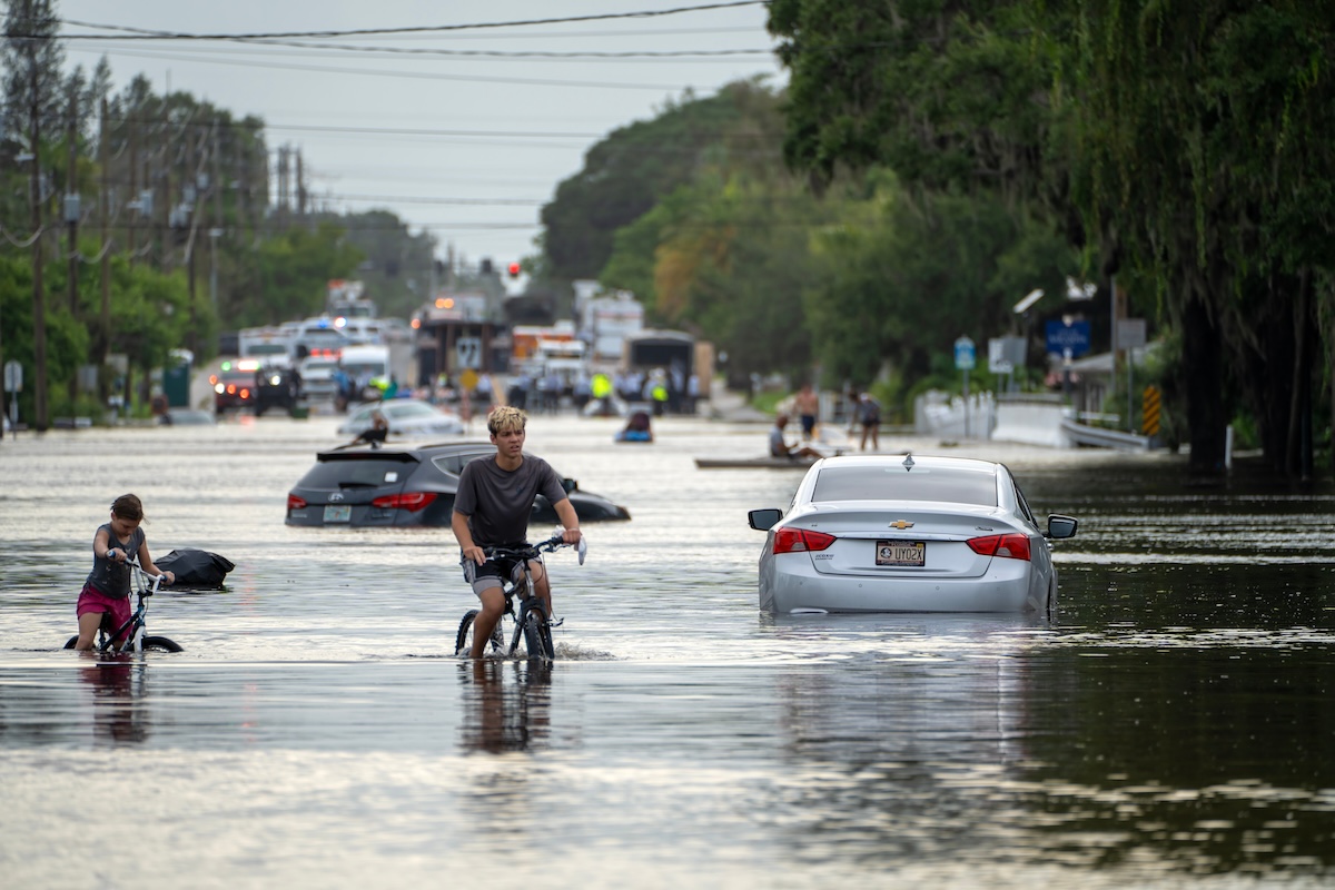 Residents bike down a flooded street. The water reaches about halfway up the bike tires.